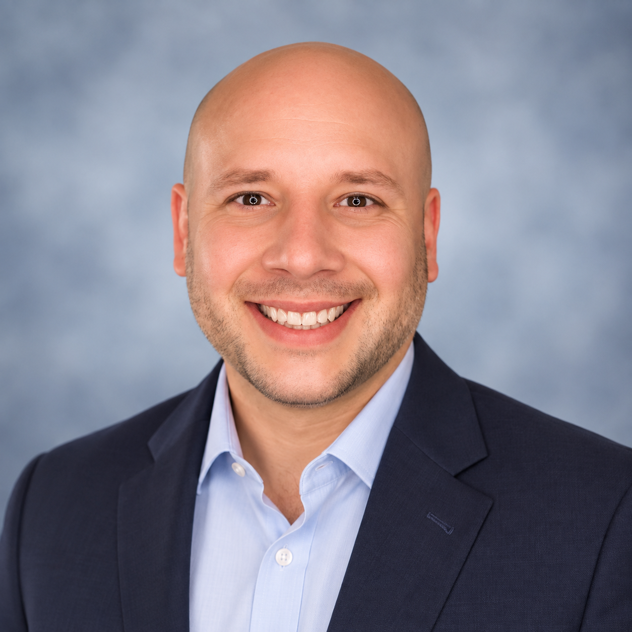 Christopher L. Garner smiling, wearing a navy jacket and an open collar blue shirt.